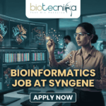 Dream Bioinformatics Job at Syngene | Associate Scientist Role You Can’t Miss! A high-tech promotional graphic for a Bioinformatics Job at Syngene, featuring the Biotecnika logo at the top. The image depicts a female scientist in a professional office setting, using a digital stylus to interact with glowing, transparent holographic screens. These displays show complex biological data, including 3D molecular protein structures, genetic heatmaps, and phylogenetic trees. In the background, a modern laboratory with other researchers is visible. The central text reads "BIOINFORMATICS JOB AT SYNGENE" in bold gold lettering, with a dark blue "APPLY NOW" button located at the bottom center.