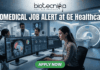 Biomedical Job at GE Healthcare Clinical Specialist Role. A professional featured image for a Biomedical Job Alert at GE Healthcare. The Biotecnika logo is positioned at the top center. The main scene shows a female biomedical professional sitting at a modern workstation with dual monitors displaying high-resolution brain scans (MRI/CT) and complex data analytics. In the background, other colleagues in white lab coats are visible in a brightly lit, high-tech clinical environment. Behind a glass partition, a large, state-of-the-art medical imaging scanner is featured. At the bottom, a prominent green button reads "APPLY NOW." The image uses a professional blue and white color palette to emphasize a cutting-edge healthcare setting.