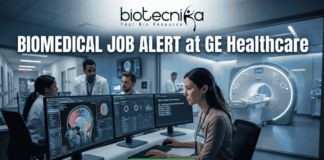Biomedical Job Alert at GE Healthcare | Exciting Job Opportunity for Graduates Biomedical Job at GE Healthcare Clinical Specialist Role. A professional featured image for a Biomedical Job Alert at GE Healthcare. The Biotecnika logo is positioned at the top center. The main scene shows a female biomedical professional sitting at a modern workstation with dual monitors displaying high-resolution brain scans (MRI/CT) and complex data analytics. In the background, other colleagues in white lab coats are visible in a brightly lit, high-tech clinical environment. Behind a glass partition, a large, state-of-the-art medical imaging scanner is featured. At the bottom, a prominent green button reads "APPLY NOW." The image uses a professional blue and white color palette to emphasize a cutting-edge healthcare setting.