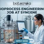 Bioprocess Engineering Job at Syngene | Biopharma Analyst Role in Bangalore | Apply Now! Bioprocess Engineering Job at Syngene Biopharma Analyst Role in Bangalore Apply Now! A professional featured image for a biotechnology job opening at Lupin. The scene depicts a female scientist in a modern, high-tech laboratory wearing a white lab coat and safety gear, working with a multichannel pipette and a multi-well plate. The background shows computer monitors with molecular structures and advanced lab equipment. The image includes the Biotecnika logo at the top center, the bold text "BIOTECHNOLOGY JOB AT LUPIN" in the middle, and a prominent "APPLY NOW" button at the bottom.