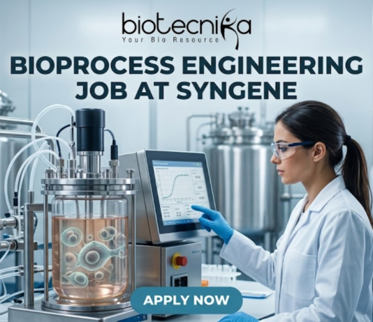 Bioprocess Engineering Job at Syngene Biopharma Analyst Role in Bangalore Apply Now! A professional featured image for a biotechnology job opening at Lupin. The scene depicts a female scientist in a modern, high-tech laboratory wearing a white lab coat and safety gear, working with a multichannel pipette and a multi-well plate. The background shows computer monitors with molecular structures and advanced lab equipment. The image includes the Biotecnika logo at the top center, the bold text "BIOTECHNOLOGY JOB AT LUPIN" in the middle, and a prominent "APPLY NOW" button at the bottom.