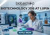 Biotechnology Job at Lupin Postgraduate Candidates Apply Now. A professional featured image for a biotechnology job opening at Lupin. The scene depicts a female scientist in a modern, high-tech laboratory wearing a white lab coat and safety gear, working with a multichannel pipette and a multi-well plate. The background shows computer monitors with molecular structures and advanced lab equipment. The image includes the Biotecnika logo at the top center, the bold text "BIOTECHNOLOGY JOB AT LUPIN" in the middle, and a prominent "APPLY NOW" button at the bottom.