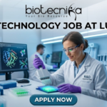 Biotechnology Job Alert! Lupin Careers Hiring Postgraduate Candidates | Apply Now Biotechnology Job at Lupin Postgraduate Candidates Apply Now. A professional featured image for a biotechnology job opening at Lupin. The scene depicts a female scientist in a modern, high-tech laboratory wearing a white lab coat and safety gear, working with a multichannel pipette and a multi-well plate. The background shows computer monitors with molecular structures and advanced lab equipment. The image includes the Biotecnika logo at the top center, the bold text "BIOTECHNOLOGY JOB AT LUPIN" in the middle, and a prominent "APPLY NOW" button at the bottom.