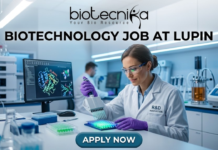 Biotechnology Job Alert! Lupin Careers Hiring Postgraduate Candidates | Apply Now Biotechnology Job at Lupin Postgraduate Candidates Apply Now. A professional featured image for a biotechnology job opening at Lupin. The scene depicts a female scientist in a modern, high-tech laboratory wearing a white lab coat and safety gear, working with a multichannel pipette and a multi-well plate. The background shows computer monitors with molecular structures and advanced lab equipment. The image includes the Biotecnika logo at the top center, the bold text "BIOTECHNOLOGY JOB AT LUPIN" in the middle, and a prominent "APPLY NOW" button at the bottom.