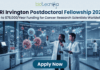 A high-tech promotional graphic for the CRI Irvington Postdoctoral Fellowship 2026, featuring the Biotecnika logo at the top. The main headline reads "CRI Irvington Postdoctoral Fellowship 2026" with a sub-headline: "Up to $78,000/Year Funding for Cancer Research Scientists Worldwide." In a futuristic, dimly lit laboratory with a night-time city skyline visible through floor-to-ceiling windows, two scientists—a woman and a man in white lab coats—interact with a large, glowing cyan holographic interface. The display shows a detailed 3D model titled "Targeted Neutralization of Cancer Cells" alongside a world map labeled "Worldwide Collaborative Data," symbolizing global research impact. At the bottom center, a prominent dark teal "Apply Now" button stands out against the sleek laboratory environment.