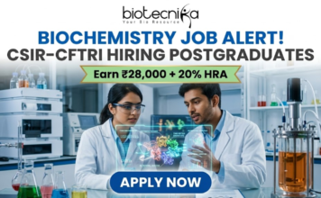 Biochemistry Job Alert! CSIR-CFTRI Hiring Postgraduates | Earn ₹28,000 + 20% HRA CSIR-CFTRI Hiring for Biochemistry Job Earn Upto ₹28,000. A professional and vibrant featured image advertisement for a biochemistry job alert at CSIR-CFTRI, created for Biotecnika. The scene features two young scientists (a man and a woman) in white lab coats and safety goggles, intensely discussing a holographic 3D molecular structure displayed over a lab bench. The background is a brightly lit, modern food science laboratory equipped with advanced bioreactors and analytical instruments. The Biotecnika logo is at the top center. The main text reads "BIOCHEMISTRY JOB ALERT! CSIR-CFTRI HIRING POSTGRADUATES" with a gold ribbon tagline below stating "Earn ₹28,000 + 20% HRA." A large, blue "APPLY NOW" button is positioned at the bottom.