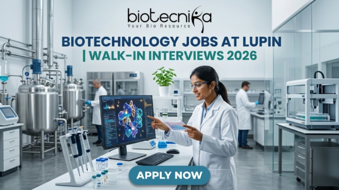 Biotechnology Jobs at Lupin | Walk-In Interviews 2026 Biotechnology Jobs at Lupin | Walk-In Interviews 2026. A high-quality, 1280x720 featured image for "Biotechnology Jobs at Lupin | Walk-In Interviews 2026." The image features the Biotecnika logo at the top center. In a modern, bright industrial laboratory, a female scientist in a white lab coat and safety goggles points to a monitor displaying a detailed 3D protein structure. Large stainless steel bioreactors and advanced lab equipment are visible in the background, creating a realistic pharmaceutical R&D atmosphere. The main title is displayed in bold teal and dark blue lettering, and a prominent blue "APPLY NOW" button is positioned at the bottom.