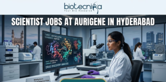 High-Paying Scientist Jobs in Hyderabad – Aurigene Hiring MSc Life Science Graduates Now! Scientist Jobs at Aurigene in Hyderabad. A high-quality, professional featured image for "Scientist Jobs at Aurigene in Hyderabad." The scene depicts a female scientist in a white lab coat and purple gloves working in a sophisticated laboratory. She is focused on a large monitor displaying vibrant 3D molecular structures under the heading "Drug Discovery Analysis." Her desk features a modern microscope and a small plaque that says "Workplace: Hyderabad Science Hub." In the background, the iconic Charminar is visible through a large window, establishing the Hyderabad setting. The Biotecnika logo is positioned at the top center, the job title is in bold white lettering, and a prominent "APPLY NOW" button is at the bottom.