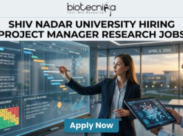 Research Jobs At Shiv Nadar University | Earn Upto ₹42,000/Month | Apply Now! Research Jobs at Shiv Nadar University | Apply Now. A high-quality, realistic featured image for a "Project Manager Research Jobs" opening at Shiv Nadar University. The scene features a professional woman in business attire interacting with a large, glowing transparent digital dashboard that displays research project timelines (Gantt charts), risk assessment matrices, and milestones for "Advanced Cell Therapy." A senior male colleague stands nearby holding a tablet with a 3D molecular visualization. The setting is a sleek, modern office with large windows overlooking a university campus at sunset. The Biotecnika logo is at the top, the main job title is in bold black text, and a prominent blue "Apply Now" button is at the bottom.