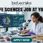 Freshers Wanted! BSc Life Sciences Job at Yogabar | Apply Now BSc Life Sciences Job at Yogabar Careers | Apply Now. A high-quality, professional featured image for a "BSc Life Sciences Job at Yogabar." The scene depicts a female food scientist in a white lab coat and safety goggles in a bright, modern food science laboratory. She is carefully examining a healthy snack bar under a professional microscope. On her desk are raw ingredients like chia seeds, flax seeds, and berries, alongside advanced lab equipment like a moisture analyzer. A large computer monitor in the background displays complex "Nutritional Profile Analysis" and 3D protein structures. The Biotecnika logo is at the top, the main job title is in bold black text, and a prominent "APPLY NOW" button is at the bottom.