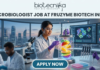 Microbiologist Job at Fruzyme Biotech India | Freshers Eligible. A professional and vibrant featured image for a "Microbiologist Job at Fruzyme Biotech India." The image depicts a female scientist in a high-tech lab working with a unique bioreactor containing glowing, levitating fruit slices, symbolizing specialized enzyme research. Modern lab equipment, data-filled monitors showing "Fruit Polysaccharide Enzyme Pathways," and a city skyline are visible in the background. The Biotecnika logo is positioned at the top center, the main title is in bold black text, and a prominent "APPLY NOW" button is at the bottom.