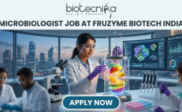 Fruzyme Biotech India Hiring Microbiologist Job | Freshers Eligible Apply Now! Microbiologist Job at Fruzyme Biotech India | Freshers Eligible. A professional and vibrant featured image for a "Microbiologist Job at Fruzyme Biotech India." The image depicts a female scientist in a high-tech lab working with a unique bioreactor containing glowing, levitating fruit slices, symbolizing specialized enzyme research. Modern lab equipment, data-filled monitors showing "Fruit Polysaccharide Enzyme Pathways," and a city skyline are visible in the background. The Biotecnika logo is positioned at the top center, the main title is in bold black text, and a prominent "APPLY NOW" button is at the bottom.