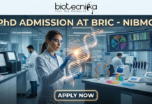 PhD Admission At BRIC – NIBMG Open Now | Life Science Graduates Apply for Fully Funded Research! PhD Admission At BRIC - NIBMG | Fully Funded Research. A sleek, high-tech professional featured image for "PhD Admission At BRIC - NIBMG." The image features a focused female researcher in a white lab coat and safety glasses, interacting with a glowing, holographic 3D DNA helix in a modern genomic laboratory. The background shows other scientists working with advanced sequencing equipment and large curved monitors displaying genomic mapping data. The Biotecnika logo is at the top center, the main title is in elegant gold and white lettering, and a glowing "APPLY NOW" button is positioned at the bottom.