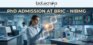 PhD Admission At BRIC – NIBMG Open Now | Life Science Graduates Apply for Fully Funded Research! PhD Admission At BRIC - NIBMG | Fully Funded Research. A sleek, high-tech professional featured image for "PhD Admission At BRIC - NIBMG." The image features a focused female researcher in a white lab coat and safety glasses, interacting with a glowing, holographic 3D DNA helix in a modern genomic laboratory. The background shows other scientists working with advanced sequencing equipment and large curved monitors displaying genomic mapping data. The Biotecnika logo is at the top center, the main title is in elegant gold and white lettering, and a glowing "APPLY NOW" button is positioned at the bottom.