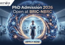 PhD Admission 2026 Open at BRIC-NBRC | Apply For Biotechnology & Neuroscience Program Today PhD Admission 2026 Open at BRIC-NBRC | Apply Online Today. A featured image for PhD Admission 2026 at BRIC-NBRC. The image shows a female scientist in a white lab coat standing in a futuristic laboratory, surrounded by a large, glowing holographic human brain with intricate neural pathways. The text "PhD Admission 2026 Open at BRIC-NBRC" is prominently displayed at the top center. The Biotecnika logo is in the top left corner, and a blue "APPLY NOW" button is positioned at the bottom. Background researchers work in a high-tech neurobiology research environment.