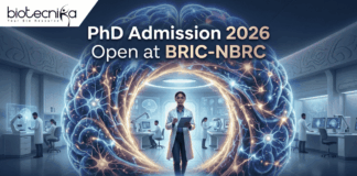 PhD Admission 2026 Open at BRIC-NBRC | Apply Online Today. A featured image for PhD Admission 2026 at BRIC-NBRC. The image shows a female scientist in a white lab coat standing in a futuristic laboratory, surrounded by a large, glowing holographic human brain with intricate neural pathways. The text "PhD Admission 2026 Open at BRIC-NBRC" is prominently displayed at the top center. The Biotecnika logo is in the top left corner, and a blue "APPLY NOW" button is positioned at the bottom. Background researchers work in a high-tech neurobiology research environment.