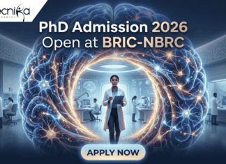 PhD Admission 2026 Open at BRIC-NBRC | Apply Online Today. A featured image for PhD Admission 2026 at BRIC-NBRC. The image shows a female scientist in a white lab coat standing in a futuristic laboratory, surrounded by a large, glowing holographic human brain with intricate neural pathways. The text "PhD Admission 2026 Open at BRIC-NBRC" is prominently displayed at the top center. The Biotecnika logo is in the top left corner, and a blue "APPLY NOW" button is positioned at the bottom. Background researchers work in a high-tech neurobiology research environment.