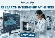 A professional featured image for a 'Research Internship at Henkel.' The visual shows a female scientist in a white lab coat and safety goggles working in a high-tech, modern laboratory. She is operating advanced analytical equipment while a large monitor in the background displays colorful 3D molecular simulations. The Biotecnika logo is placed at the top, and a prominent 'Apply Now' button is located at the bottom center.