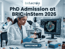 A high-resolution featured image for PhD Admission at BRIC-inStem 2026. The image depicts a modern, realistic biotechnology laboratory where a female scientist of Indian descent, wearing a lab coat and safety goggles, is carefully examining a multi-well plate. Beside her, a computer monitor displays a vibrant, high-detail microscopic image of a stem cell labeled with genetic markers. The Biotecnika logo is positioned at the top center, and a prominent "APPLY NOW" button is located at the bottom.