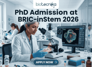 PhD Admission at BRIC-inStem 2026 | JRF-Based Entry + Cutting-Edge Stem Cell Research Opportunity! A high-resolution featured image for PhD Admission at BRIC-inStem 2026. The image depicts a modern, realistic biotechnology laboratory where a female scientist of Indian descent, wearing a lab coat and safety goggles, is carefully examining a multi-well plate. Beside her, a computer monitor displays a vibrant, high-detail microscopic image of a stem cell labeled with genetic markers. The Biotecnika logo is positioned at the top center, and a prominent "APPLY NOW" button is located at the bottom.