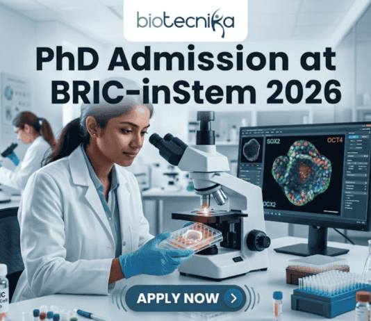 A high-resolution featured image for PhD Admission at BRIC-inStem 2026. The image depicts a modern, realistic biotechnology laboratory where a female scientist of Indian descent, wearing a lab coat and safety goggles, is carefully examining a multi-well plate. Beside her, a computer monitor displays a vibrant, high-detail microscopic image of a stem cell labeled with genetic markers. The Biotecnika logo is positioned at the top center, and a prominent "APPLY NOW" button is located at the bottom.
