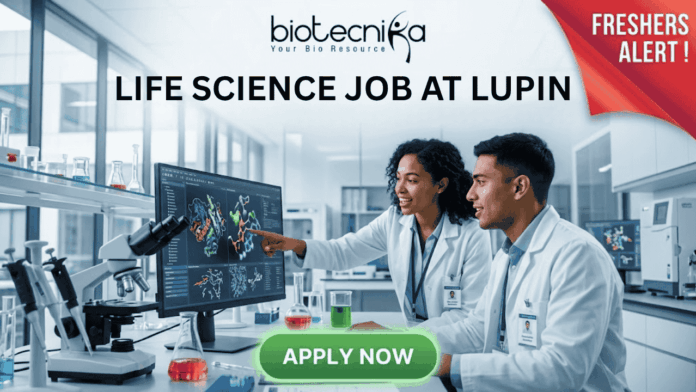 Freshers Alert! Life Science Job at Lupin | Graduates Apply Now. Featured image for a Life Science job opening at Lupin, featuring two young scientists in a modern laboratory. One scientist points at a high-tech monitor displaying colorful 3D protein structures while they collaborate. The image includes the Biotecnika logo at the top, a red "FRESHERS ALERT!" banner in the top right corner, and a prominent green "APPLY NOW" button at the bottom. Central text reads: "LIFE SCIENCE JOB AT LUPIN - Build Your Career with a Leading Pharmaceutical Leader."