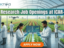 25+ Research Job Openings at ICAR-IARI – Online Interview . A featured image for a job advertisement titled "25+ Research Job Openings at ICAR-IARI." The image depicts a futuristic, high-tech agricultural laboratory set within a large glass greenhouse. In the foreground, a female and a male scientist in white lab coats are working at a digital station, examining young green plants. Digital screens display DNA sequences and plant growth data. In the background, a drone flies over rows of crops, and through the glass walls, traditional farmers are seen working in lush green fields. The Biotecnika logo is at the top left, and a prominent orange "APPLY NOW" button is centered at the bottom.