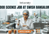 Food Science Job at Swish Bangalore. A clean, modern featured image showing a food scientist in a sterile lab environment using a precision pipette on a nutrient-rich food prototype. The lab is equipped with advanced food testing machinery and colorful test tubes. The city skyline of Bangalore is visible through the window. The Biotecnika logo is at the top, and an orange "Apply Now" button is at the bottom.
