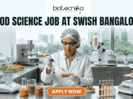 Food Science Job at Swish Bangalore. A clean, modern featured image showing a food scientist in a sterile lab environment using a precision pipette on a nutrient-rich food prototype. The lab is equipped with advanced food testing machinery and colorful test tubes. The city skyline of Bangalore is visible through the window. The Biotecnika logo is at the top, and an orange "Apply Now" button is at the bottom.