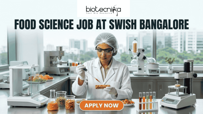 at Swish Bangalore Food Science Job at Swish Bangalore. A clean, modern featured image showing a food scientist in a sterile lab environment using a precision pipette on a nutrient-rich food prototype. The lab is equipped with advanced food testing machinery and colorful test tubes. The city skyline of Bangalore is visible through the window. The Biotecnika logo is at the top, and an orange "Apply Now" button is at the bottom.