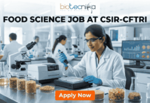 Latest Food Science Job Alert: CSIR-CFTRI Hiring Project Associate | Earn Upto ₹31,000 + HRA Food Science Job at CSIR-CFTRI Earn Upto ₹31,000 + HRA. A professional recruitment banner for a Food Science job at CSIR-CFTRI. The image features a female scientist in a white lab coat and safety glasses working in a modern, brightly lit laboratory. She is using a pipette to analyze samples in a multi-well plate. The foreground displays glass jars filled with various grains and food ingredients. The Biotecnika logo is at the top center, and the main text reads "FOOD SCIENCE JOB AT CSIR-CFTRI" in bold black letters. A prominent orange "Apply Now" button is positioned at the bottom.