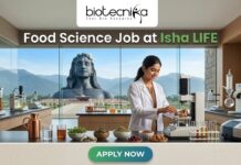 Exciting Food Science Job Alert: Join Isha LIFE as R&D Specialist Today!! Food Science Job at Isha LIFE R&D Specialist Role. A featured image for a job posting titled "Food Science Job at Isha LIFE." The image displays a professional female scientist in a white lab coat working in a modern, high-tech food laboratory. On the lab counter, there are various bowls of natural grains, herbs, and scientific testing equipment. Through the large glass windows in the background, the iconic Adi Yogi statue is visible against a scenic mountain landscape, reflecting the Isha Foundation theme. The Biotecnika logo is positioned at the top center, and a prominent green "APPLY NOW" button is located at the bottom.