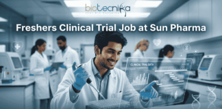 Clinical Trial Job Alert: Freshers Wanted at Sun Pharma – Start Your Clinical Research Career Today! Freshers Clinical Trial Job at Sun Pharma | Don't Miss It. A featured image for a job posting titled "Freshers Clinical Trial Job at Sun Pharma" in a $1280 \times 720$ format.The image depicts a modern, high-tech laboratory setting where a young, smiling male scientist in a white lab coat is working with a pipette and a multi-well plate. A transparent digital holographic display in front of him shows "Clinical Trial Data" with various charts and graphs. In the background, other researchers are visible in a clean, professional clinical environment.The Biotecnika logo is positioned clearly at the top center, and a prominent, rounded "APPLY NOW" button is located at the bottom center. The overall aesthetic is professional, bright, and engaging.