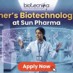 Fresher's Job Alert! Biotechnology Job at Sun Pharma Don’t Miss Out! A promotional job banner with the Biotecnika logo at the top. The headline text is "Fresher's Biotechnology Job" and "at Sun Pharma". A smiling young woman in a lab coat stands in a futuristic laboratory, interacting with floating holographic screens. The screens display molecular structures labeled "Drug Discovery" and "Lead Identification," and a DNA helix with graphs labeled "DNA" and "Data Discovery". A large red button at the bottom says "Apply Now". The background shows complex lab equipment.