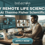 Fully Remote Life Science Job at Thermo Fisher Scientific – Global Opportunity! A professional, attractive, and unique featured image for a "Fully Remote Life Science Job At Thermo Fisher Scientific," recruited through biotecnika. A smiling South Asian man with headphones types on a laptop at a large wooden desk in a bright home office. His desk features monitors displaying 3D molecular structures, data charts, and a group video conference call. Automated lab equipment and reagent tubes are on the desk. A large window overlooks a scenic mountainous view, with a tabby cat asleep nearby. Header text reads 'FULLY REMOTE LIFE SCIENCE JOB At Thermo Fisher Scientific'. The 'biotecnika Your Bio Resource' logo is at the top. A prominent 'APPLY NOW' button is at the bottom center. No Thermo Fisher Scientific company logo graphic is present.