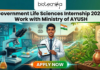 Government Life Sciences Internship 2026 at CCIH | Work with Ministry of AYUSH Government Life Sciences Internship 2026 Work with Ministry of AYUSH. A featured image for Biotecnika Global promoting a "Government Life Sciences Internship 2026: Work with Ministry of AYUSH." The graphic features a young male scientist in a white lab coat standing at the center, holding a digital tablet. The background is a vibrant blend of modern biotechnology—showing molecular models and lab equipment—and traditional Indian medicine, featuring medicinal herbs, a Tulsi plant, and a stone mortar and pestle. In the distance, a grand government building flies the Indian national flag. The top of the image displays the Biotecnika logo, and a prominent orange "APPLY NOW" button is centered at the bottom.