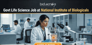 Govt Life Science Job Alert 2026 at National Institute of Biologicals. A professional featured image for a "Govt Life Science Job at National Institute of Biologicals." It shows a scientist in a clean, modern laboratory setting operating a bioreactor. The design features a prominent Biotecnika logo at the top, the Indian national emblem (Satyameva Jayate) in a frame on the desk, and a bright orange "Apply Now" button at the bottom.