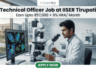 High-Paying Technical Officer Job at IISER Tirupati – Get Monthly Emoluments of ₹57,000 + 9% HRA High-Paying Technical Officer Job at IISER Tirupati – Apply Before Deadline!. A professional recruitment graphic for a Technical Officer job at IISER Tirupati. The image features a focused male scientist in a modern, brightly lit laboratory environment, working with high-tech equipment and dual monitors displaying colorful microscopic cell images. At the top, the Biotecnika logo is positioned above bold text that reads: "Technical Officer Job at IISER Tirupati" with a tagline "Earn Upto ₹57,000 + 9% HRA/ Month." A prominent green "Apply Now" button is located at the bottom center.