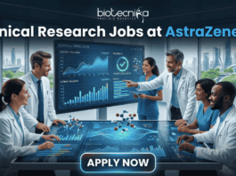 Hiring Now! Clinical Research Jobs at AstraZeneca for Life Science Graduates! A professional featured image for "Clinical Research Jobs at AstraZeneca." It shows a group of medical researchers in lab coats gathered around a large interactive touch-table displaying clinical trial data, graphs, and 3D molecular models. The Biotecnika logo is at the top, and a sleek "Apply Now" button is at the bottom.