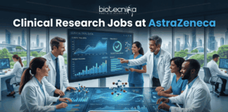 Hiring Now! Clinical Research Jobs at AstraZeneca for Life Science Graduates! A professional featured image for "Clinical Research Jobs at AstraZeneca." It shows a group of medical researchers in lab coats gathered around a large interactive touch-table displaying clinical trial data, graphs, and 3D molecular models. The Biotecnika logo is at the top, and a sleek "Apply Now" button is at the bottom.
