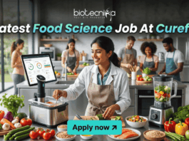 Latest Food Science Job At Curefit Apply For Nutritionist Role. A sleek, lifestyle-oriented featured image for "Latest Food Science Job At Curefit." It shows a food scientist in a modern culinary lab using smart kitchen technology like a sous-vide machine and a tablet dashboard. The Biotecnika logo is at the top, and a cyan "Apply now" button is at the bottom.