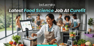 Latest Food Science Job At Curefit Apply For Nutritionist Role. A sleek, lifestyle-oriented featured image for "Latest Food Science Job At Curefit." It shows a food scientist in a modern culinary lab using smart kitchen technology like a sous-vide machine and a tablet dashboard. The Biotecnika logo is at the top, and a cyan "Apply now" button is at the bottom.