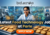 Latest Food Technology Job at Parle – BSc & BTech Graduates Apply Now. An advertisement featuring a smiling woman in a lab coat and safety glasses, working in a food production environment surrounded by futuristic holographic displays of "FLAVOR COMPOUNDS" and "NUTRIENT CHAINS." Large text reads "Latest Food Technology Job at Parle." At the top is the "biotecnika Your Bio Resource" logo, and a large "APPLY NOW" button is at the bottom. Trays of biscuits are on the counter.