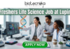 Latest Life Science Job at Lupin Freshers Welcome to Apply. A professional 1280x720 featured image for a "Freshers Life Science Job at Lupin." The Biotecnika logo is placed at the top center. The main heading reads "Freshers Life Science Job at Lupin" in a bold, clean font. The background features a realistic, high-tech laboratory where three enthusiastic young scientists—two women and one man—are collaborating and smiling. One scientist is pointing toward a large monitor displaying detailed 3D protein structures and genomic data. The lab environment is bright and modern, filled with scientific equipment like microscopes and pipettes. At the bottom, a prominent green "APPLY NOW" button encourages viewers to take action.