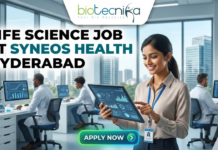 Exciting Life Science Job at Syneos Health Hyderabad | BSc/MSc Candidates Apply Now Life Science Job at Syneos Health Hyderabad. A career advertisement banner for a life science job at Syneos Health in Hyderabad, presented by Biotecnika Global. The banner features a smiling woman in a lab coat and safety glasses, holding and pointing at a tablet that displays data charts and a molecular structure. She is standing in a modern office and laboratory setting, with large windows overlooking a city skyline. Other researchers in lab coats are seated at desks in the background, working on computer monitors. The "biotecnika Global Hiring and Neurnic Solutions" logo is at the top, and a green "Apply now" button with an arrow is at the bottom.