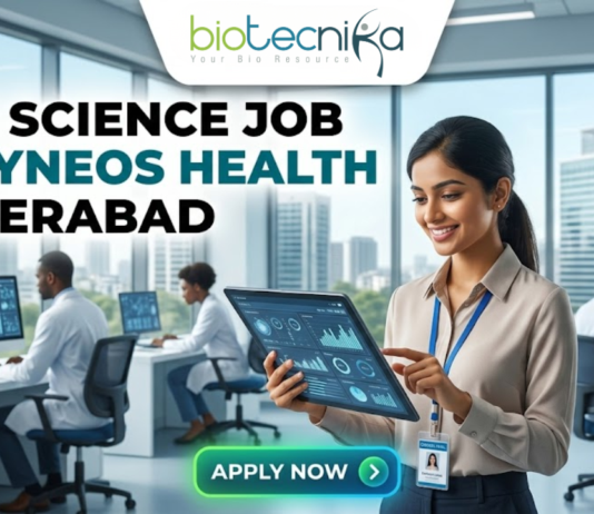 Life Science Job at Syneos Health Hyderabad. A career advertisement banner for a life science job at Syneos Health in Hyderabad, presented by Biotecnika Global. The banner features a smiling woman in a lab coat and safety glasses, holding and pointing at a tablet that displays data charts and a molecular structure. She is standing in a modern office and laboratory setting, with large windows overlooking a city skyline. Other researchers in lab coats are seated at desks in the background, working on computer monitors. The "biotecnika Global Hiring and Neurnic Solutions" logo is at the top, and a green "Apply now" button with an arrow is at the bottom.