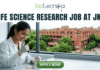Life Science Research Job At Jawaharlal Nehru University (JNU). A high-quality featured image for a job page (1280x720) with the "biotecnika" logo and text at the top. Large, clear text reads: "MSc LIFE SCIENCE FRESHERS JOB at Thermo Fisher Scientific". Imagery shows a diverse group of four young scientists in lab coats and stylish casual wear collaborating enthusiastically around a transparent screen displaying a colourful 3D molecular model, within a sophisticated, sunlit laboratory. The background features unbranded lab equipment and natural light. A distinct green rectangular button at the bottom center has the text "Apply Now", with smaller text "MSc LIFE SCIENCE FRESHERS JOB" below it. The entire top section is framed by a deep teal textured banner. The scene is realistic, attractive, and conveys energy and discovery, suitable for going viral.