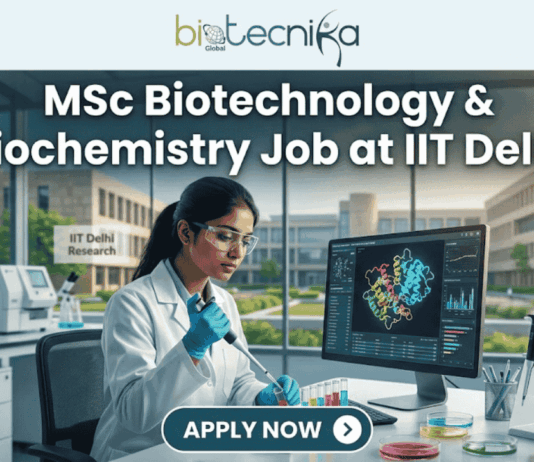 MSc Biotechnology & Biochemistry Job at IIT Delhi. A professional and realistic featured image for a job opening. At the top center is the Biotecnika Global logo, followed by large, bold text reading "MSc Biotechnology & Biochemistry Job at IIT Delhi." The central scene depicts a female researcher in a white lab coat working in a high-tech laboratory, using a pipette on colorful samples while viewing a 3D molecular structure on a large monitor. The background shows advanced lab equipment and a clear view of the IIT Delhi Research campus through large windows. At the bottom, there is a prominent teal button that says "APPLY NOW" with a white arrow icon.