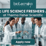 MSc Life Science Job Alert | Thermo Fisher Scientific is Hiring Freshers! MSc Life Science Job Alert Thermo Fisher Scientific is Hiring Freshers! A featured job post graphic with a realistic photo of five diverse scientists collaborating in a modern, well-equipped life science laboratory. At the top of the image, there is a dark green-blue banner featuring the 'biotecnika' logo with the tagline 'Your Bio Resource' in white. Below the logo, large, bold white text reads: 'MSc LIFE SCIENCE FRESHERS JOB at Thermo Fisher Scientific'. The background photo shows the scientists interacting with a futuristic, holographic protein molecule display, with lab equipment like beakers and bioreactors visible. At the bottom center, a distinct dark teal rectangular button has the text 'Apply now' in bold white. The image is 1280x720 pixels and has a professional, engaging design.