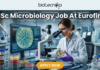 MSc Microbiology Job Alert Eurofins Hiring Research Scientists in Bengaluru – Apply Now! A high-quality, professional featured image for an "MSc Microbiology Job At Eurofins." The image features a female microbiologist in a white lab coat and purple gloves, carefully examining a petri dish containing a microbial culture. She is working at a modern lab bench equipped with a high-end microscope and a computer monitor displaying a digital analysis of a bacterial colony. The laboratory background is clean and advanced, with signs indicating "ISO 17025 ACCREDITED." The Biotecnika logo is prominent at the top center, the main job title is displayed in bold white text, and a vibrant orange "APPLY NOW" button is positioned at the bottom.